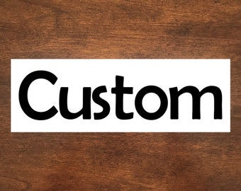 May include: White sign with black text that reads "Custom" on a brown wood background.