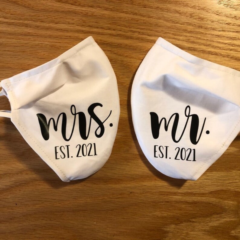 Pu&ograve; includere: Due maschere di stoffa bianche con testo nero. Una maschera dice "mrs. EST. 2021" e l'altra dice "mr. EST. 2021".