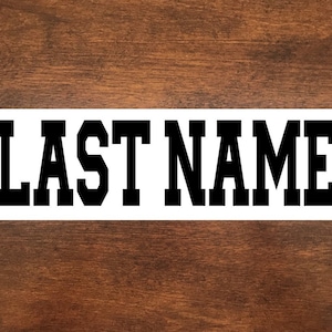 May include: White rectangular sign with black text that reads "LAST NAME" in a bold, blocky font.