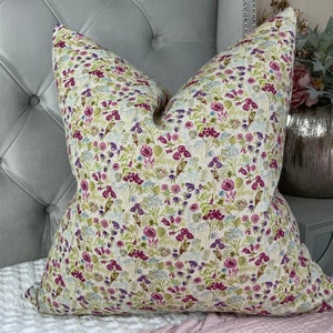 May include: A cream-colored pillow with a floral pattern featuring pink, purple, and green flowers. The pillow is made of a soft, textured fabric.