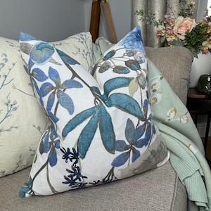May include: A white cushion with a blue and teal floral pattern. The cushion is sitting on a sofa with a light green throw blanket.