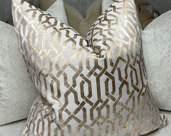 Könnte beinhalten: Ein Set dekorativer Kissen mit einem geometrischen Muster in Beige- und Goldtönen. Die Kissen sind aus einem weichen, luxuriösen Stoff gefertigt und haben einen dezenten Glanz.