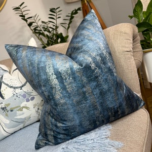May include: A blue and gold patterned throw pillow with a soft, velvety texture. The pillow is sitting on a beige couch.