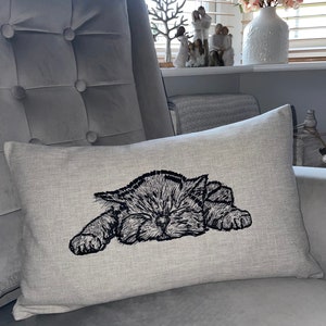 May include: A gray linen pillow with a black embroidered image of a sleeping kitten.