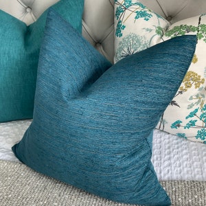Könnte beinhalten: Drei dekorative Kissen mit einem tealblauen, weißen und grünen Blumenmuster. Die Kissen sind auf einem grauen Sofa angeordnet.