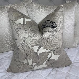 May include: A decorative throw pillow with a floral pattern in shades of gray and black on a white background. The pillow is made of a soft, luxurious fabric.