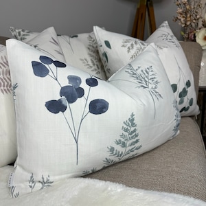 Könnte beinhalten: Vier Kissen mit weißem Hintergrund und einem blauen und grünen Blumenmuster. Die Kissen liegen auf einem braunen Sofa.