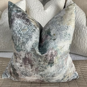 May include: A decorative throw pillow with a white background and abstract patterns in shades of gray, green, and pink.
