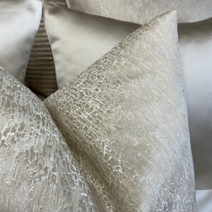 May include: Three decorative throw pillows with a textured, shimmery fabric in a light beige color.