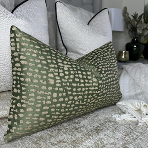 May include: A green and gold patterned throw pillow with a subtle sheen. The pillow is on a white bed with other pillows.