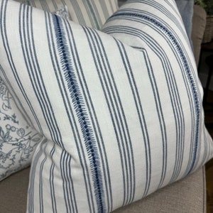 May include: White and blue striped throw pillow with a decorative stitch detail. The pillow is made of a soft, woven fabric.