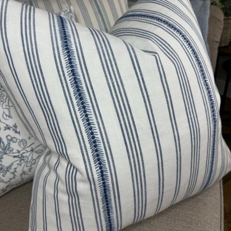 May include: White and blue striped throw pillow with a decorative stitch detail. The pillow is made of a soft, woven fabric.