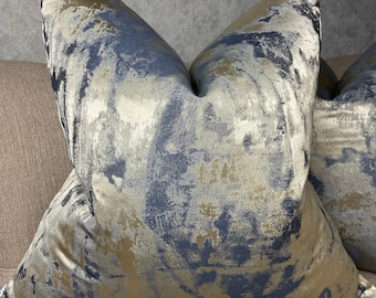 Pode incluir: Duas almofadas decorativas com um padrão abstrato azul e dourado. As almofadas são feitas de um tecido macio e texturizado.
