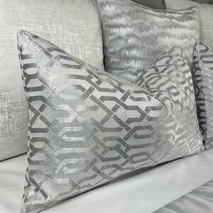 Può includere: Un set di cuscini decorativi in ​​diverse tonalità di grigio. I cuscini presentano diversi motivi, tra cui un design geometrico e un motivo astratto sottile.