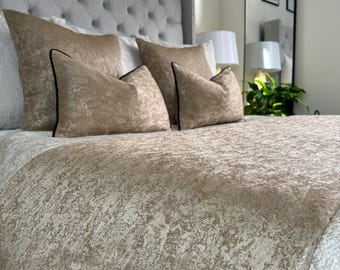 May include: A close-up of a bed with a gray headboard and a beige, textured duvet cover. The bed is made with several beige pillows with black trim.