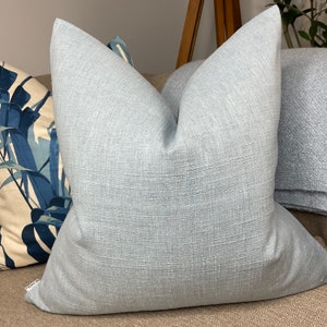May include: A light blue throw pillow with a textured fabric. The pillow is sitting on a brown couch.