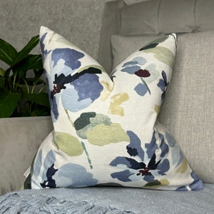 May include: A white throw pillow with a floral pattern in shades of blue, green, and yellow. The pillow is made of a soft, textured fabric and has a square shape.