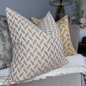 May include: Two throw pillows with geometric patterns. One pillow is a beige and white chevron pattern, and the other is a yellow and white geometric pattern.