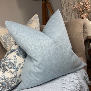 Könnte beinhalten: Ein hellblaues Kissen mit strukturiertem Stoff. Das Kissen liegt auf einem Sofa mit anderen Kissen und einer Decke.
