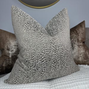 May include: A grey and white patterned throw pillow with a subtle shimmer. The pillow is made of a soft, textured fabric and has a square shape.