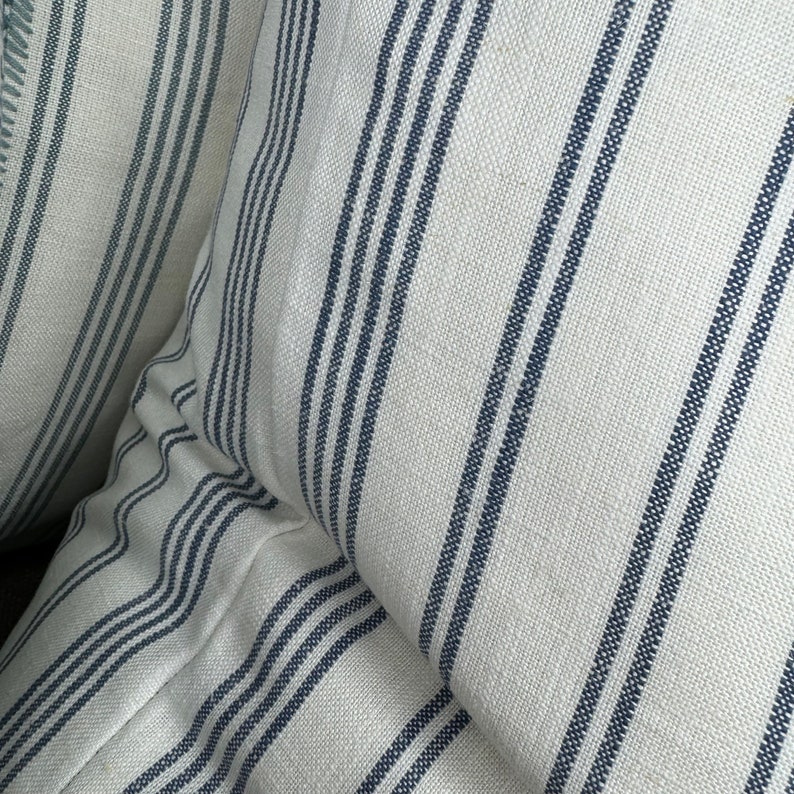May include: Two white and blue striped pillow covers with a subtle texture. The stripes are a dark blue color and are evenly spaced.