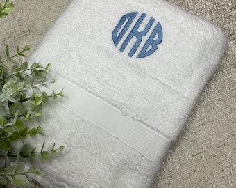 May include: White bath towel with a blue embroidered monogram of the letters "OKB" in a circle.