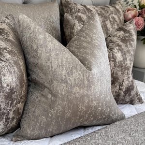 May include: Three decorative throw pillows with a textured, grey and white pattern. The pillows are arranged on a bed with a grey and white patterned bedspread.
