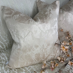 May include: Two decorative throw pillows with a white and beige abstract pattern. The pillows are made of a soft, luxurious fabric and have a subtle sheen.