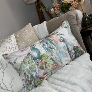 May include: A long rectangular throw pillow with a watercolor design of peacocks and tropical leaves in shades of blue, green, pink, and white.
