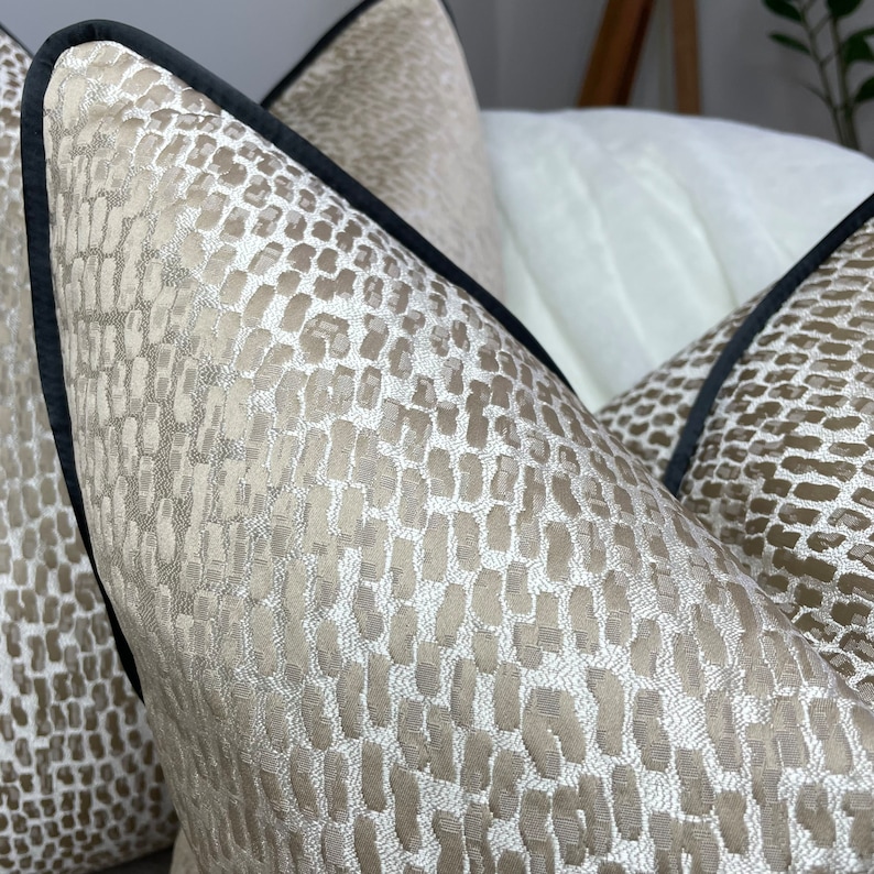 May include: Two decorative throw pillows with a beige and brown geometric pattern. The pillows have a black trim around the edges.