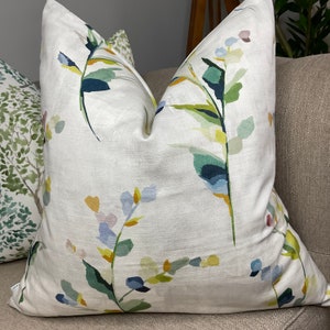 May include: A white throw pillow with a floral pattern featuring green, blue, and yellow watercolor-style leaves and flowers.