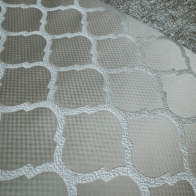 May include: A close-up of a grey fabric with a white geometric pattern. The fabric has a subtle texture and a soft, luxurious feel.