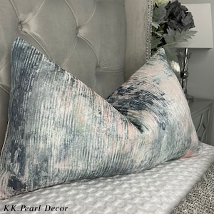 May include: A pair of decorative throw pillows with a gray and pink abstract pattern. The pillows are on a gray tufted headboard.
