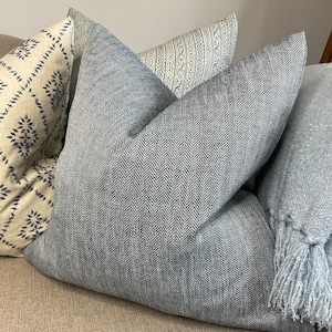 May include: A set of four decorative throw pillows with a variety of patterns. The pillows are made of a soft, textured fabric and feature a herringbone pattern, a geometric pattern, and a striped pattern. The pillows are a mix of light gray and beige colors.