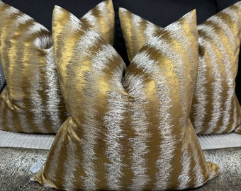 May include: Three decorative throw pillows with a gold and silver geometric pattern. The pillows are arranged on a black and silver patterned couch.