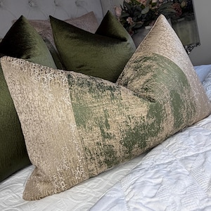 May include: Decorative pillows in shades of green and beige. One pillow features a textured, abstract design with a vertical stripe of olive green and a beige section. Other pillows are solid olive green. The pillows are on a white quilted bedspread.