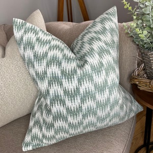 Puede incluir: Una almohada de tiro verde y blanca con un diseño geométrico. La almohada está en un sofá marrón.
