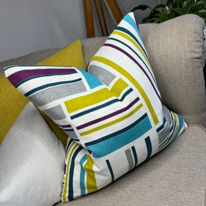 May include: A white, yellow, teal, purple, and gray striped throw pillow with a geometric pattern.