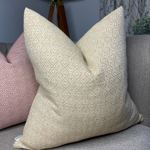 May include: A yellow and white patterned throw pillow with a geometric design. The pillow is on a grey sofa.