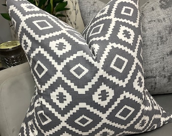 May include: Gray and white geometric patterned throw pillow with a diamond pattern. The pillow is on a gray couch.