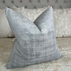 May include: A gray throw pillow with a subtle, textured pattern. The pillow is made of a soft, luxurious fabric and is perfect for adding a touch of elegance to any room.