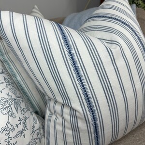 May include: A white and blue striped pillow with a blue stitched border. The pillow is made of a soft, textured fabric.