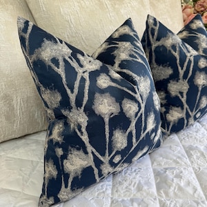 May include: Three navy blue cushions with a silver floral pattern. The cushions are arranged on a white bedspread. The cushions have a square shape and are made of a soft, textured fabric. The floral design adds a touch of elegance to the cushions.