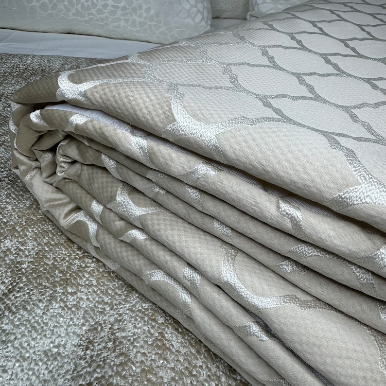 May include: A folded beige throw blanket with an embroidered geometric pattern. The blanket is made of a soft, luxurious fabric and is perfect for adding a touch of elegance to any room.