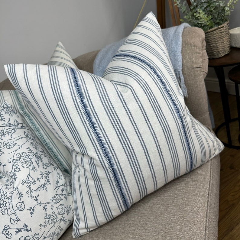 May include: Two decorative throw pillows with a white background and blue stripes. The pillows have a subtle blue stitching detail around the edges.