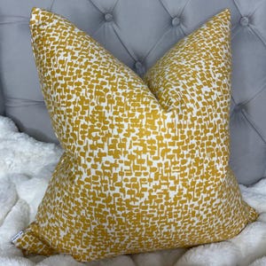 May include: A yellow and white patterned cushion with a geometric design. The cushion is on a grey tufted sofa.