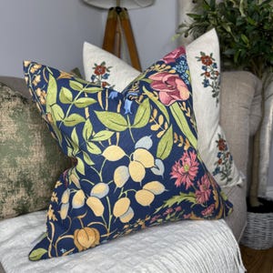 May include: A navy blue throw pillow with a floral pattern featuring yellow, pink, and green flowers. The pillow is on a couch with other pillows.