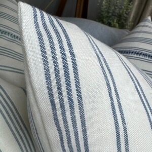 May include: Two white and blue striped throw pillows with a subtle woven texture. The pillows have a simple, classic design.