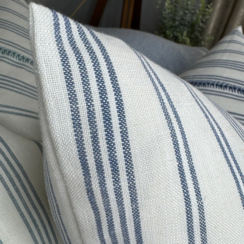 May include: Two white and blue striped throw pillows with a subtle woven texture. The pillows have a simple, classic design.