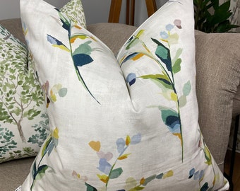 Könnte beinhalten: Ein weißes Kissen mit einem floralen Muster in Blautönen, Grün, Gelb und Orange. Das Kissen ist aus einem weichen, strukturierten Stoff gefertigt und hat einen dezenten Glanz.